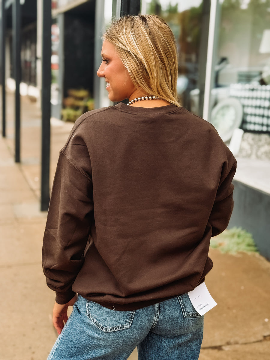 Woman on city street wearing dark brown sweatshirt with metallic bronze horse bit logo