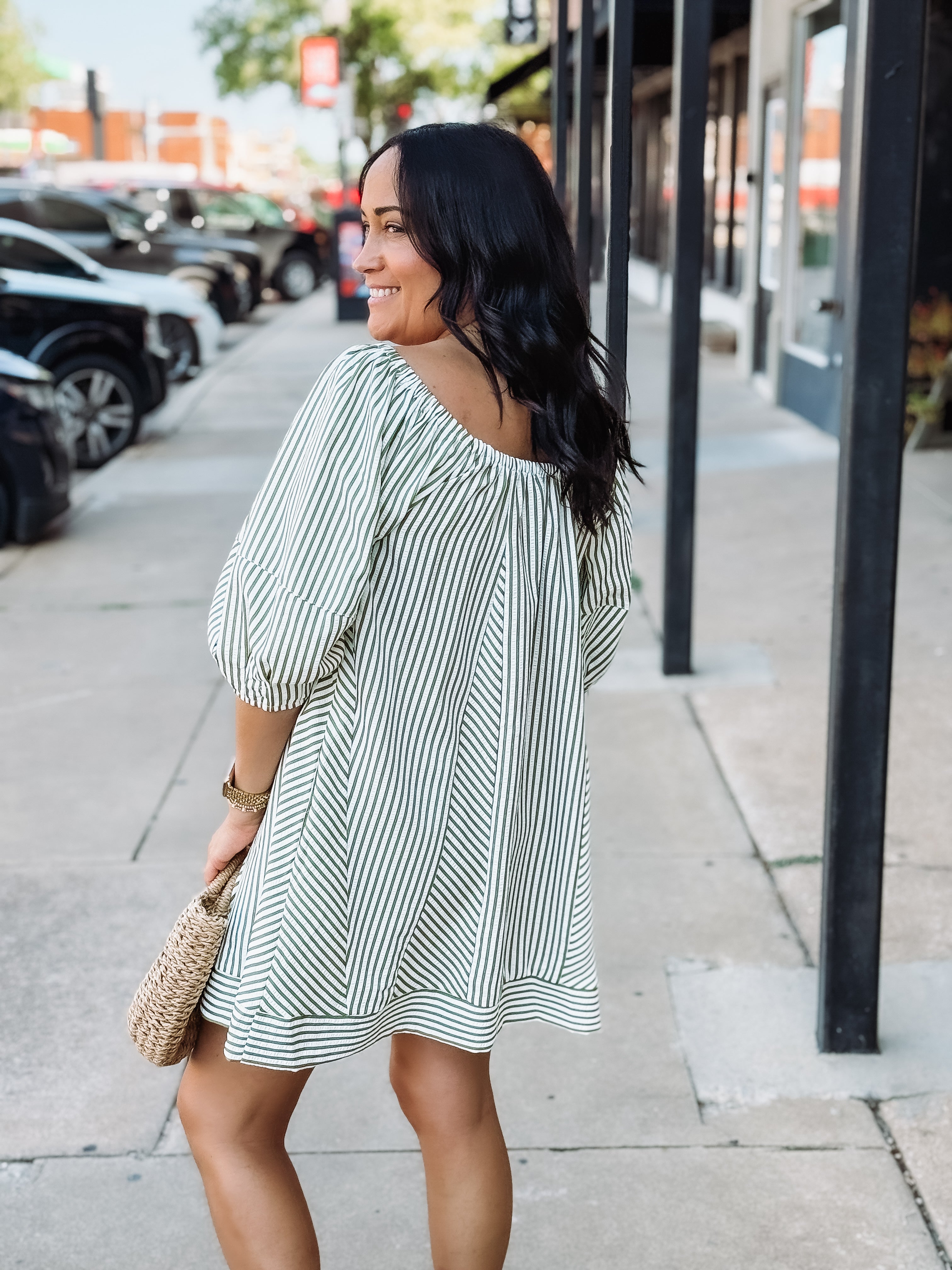 Woman in a striped dress walking on a sidewalk with cars and buildings in the background