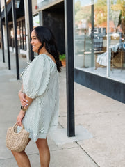Woman in a striped dress holding a straw bag on a sidewalk.