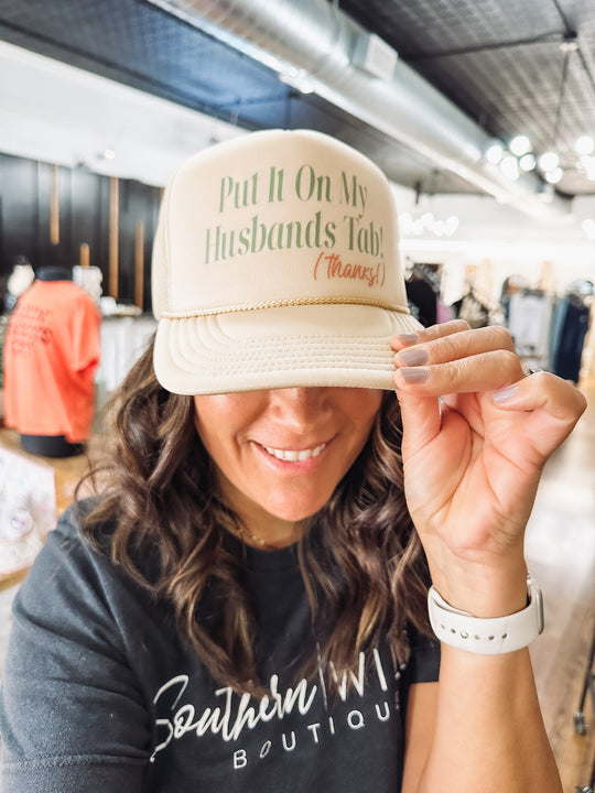 Pink and olive green "Put it on My Husband's Tab" typography on khaki Otto trucker.