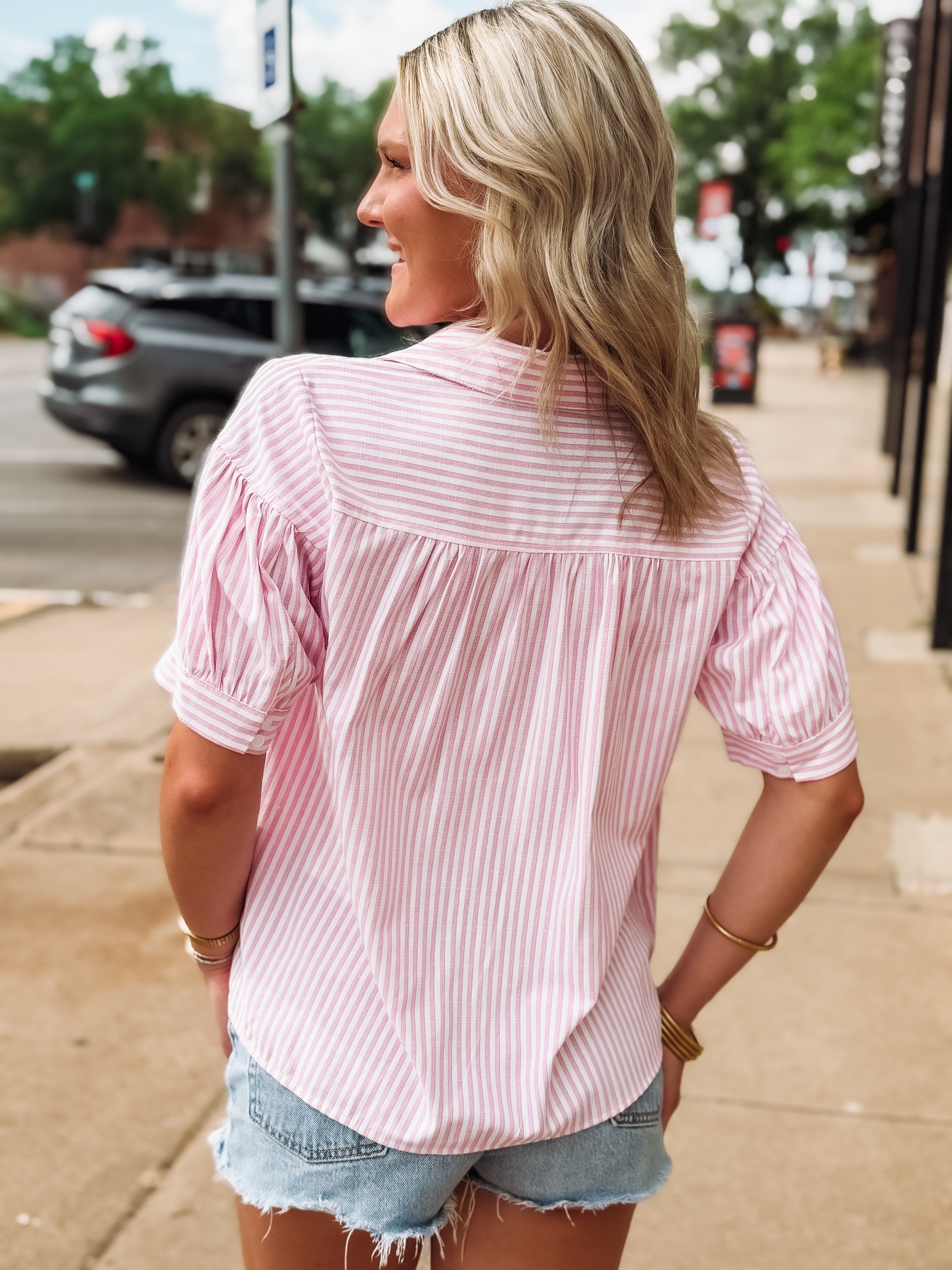 Woman wearing a pink striped shirt and denim shorts on a sidewalk.