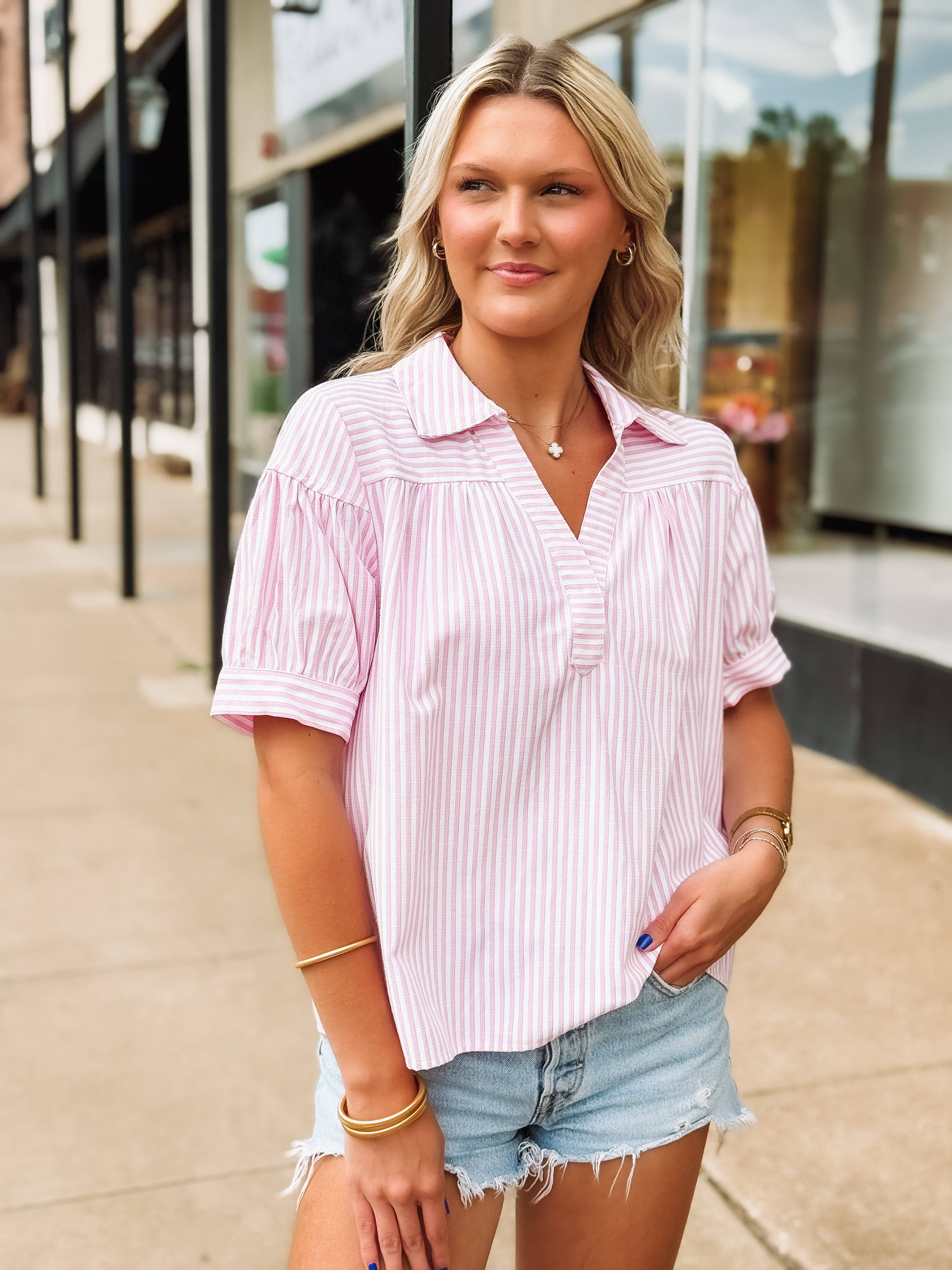 Woman wearing a pink and white striped shirt and denim shorts outdoors.