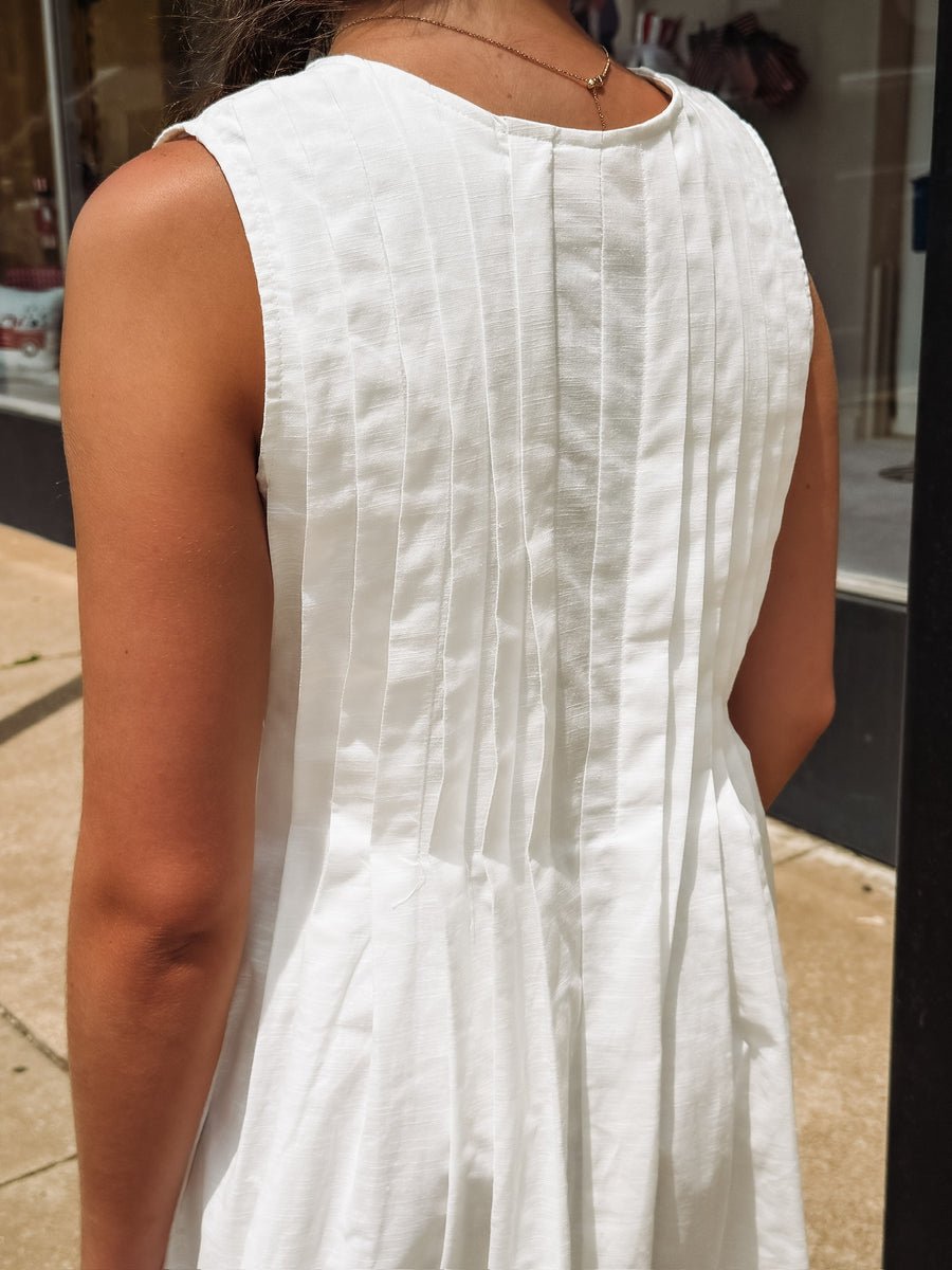 White sleeveless pleated mini dress with bow tie details.