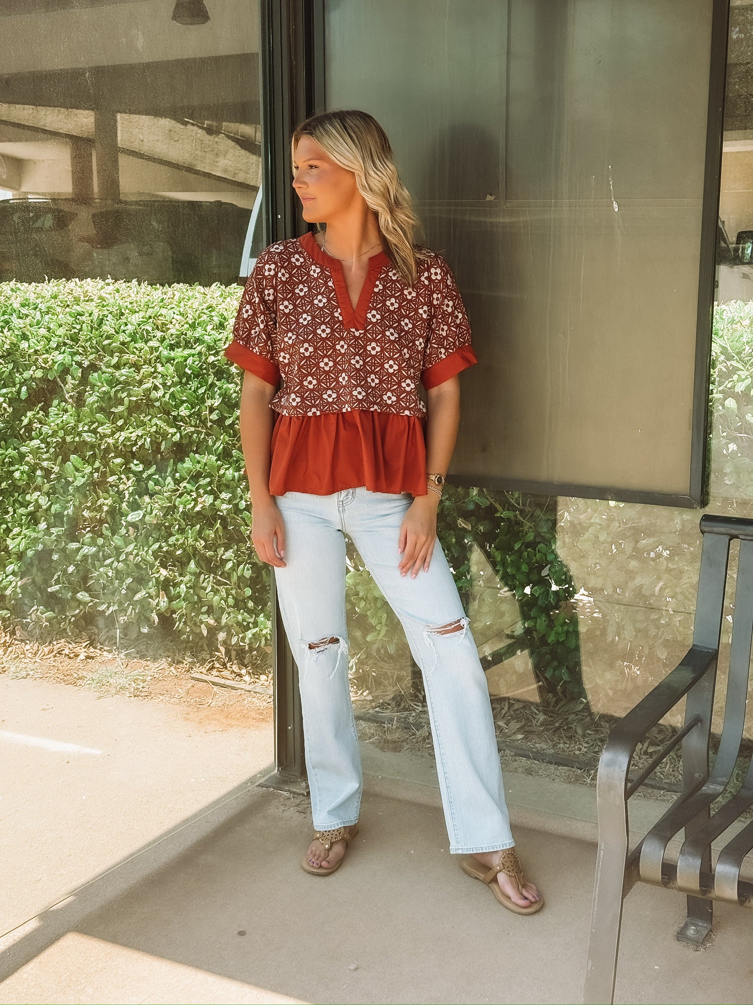 Rust colored short sleeve top with a peplum hem and a mixed media white floral pattern up top.