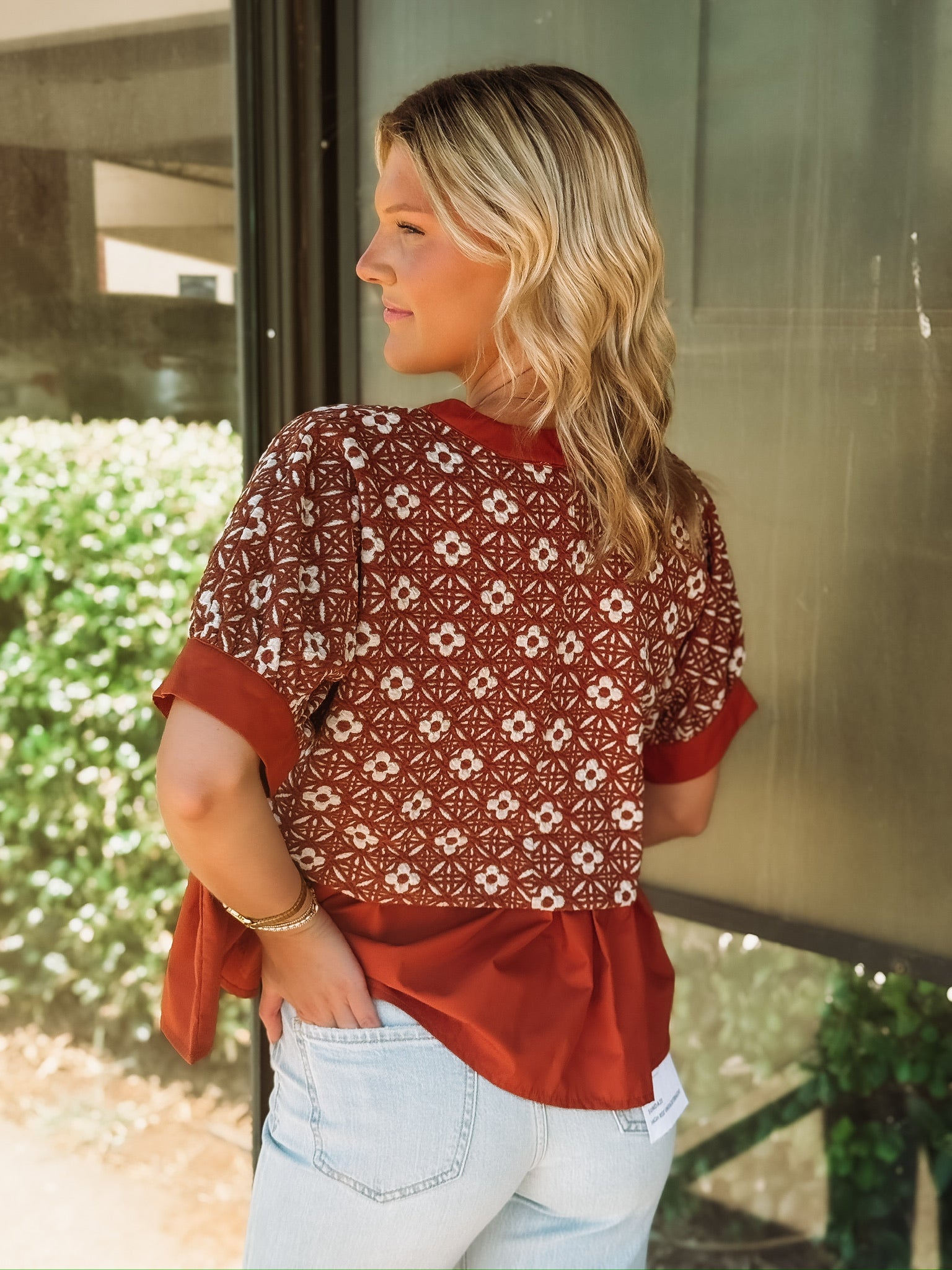 Rust colored short sleeve top with a peplum hem and a mixed media white floral pattern up top.