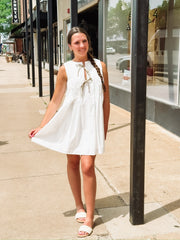 White sleeveless pleated mini dress with bow tie details.