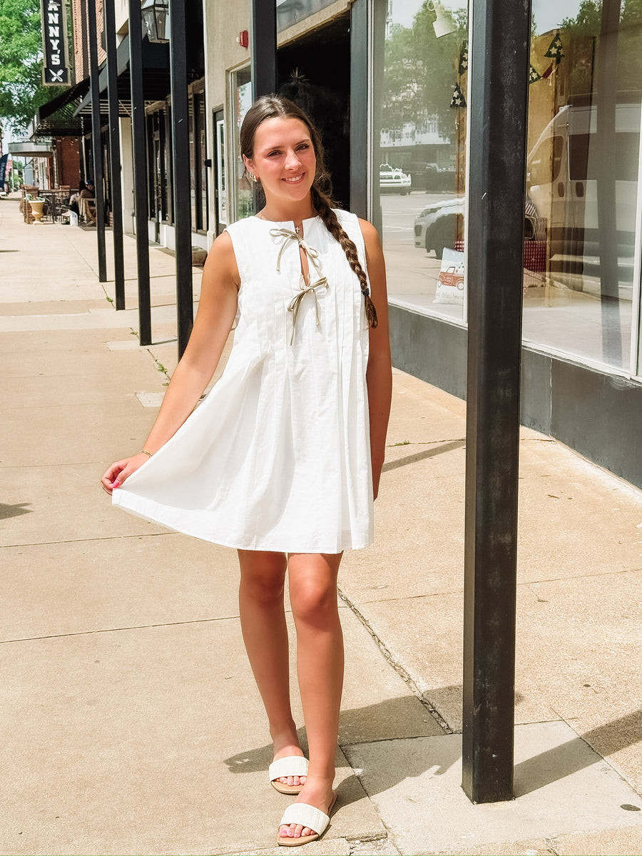 White sleeveless pleated mini dress with bow tie details.