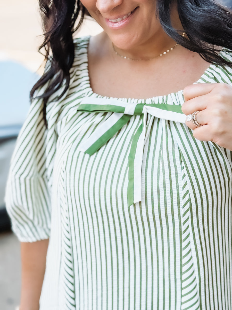 Woman wearing a green and white striped dress with a green ribbon detail.