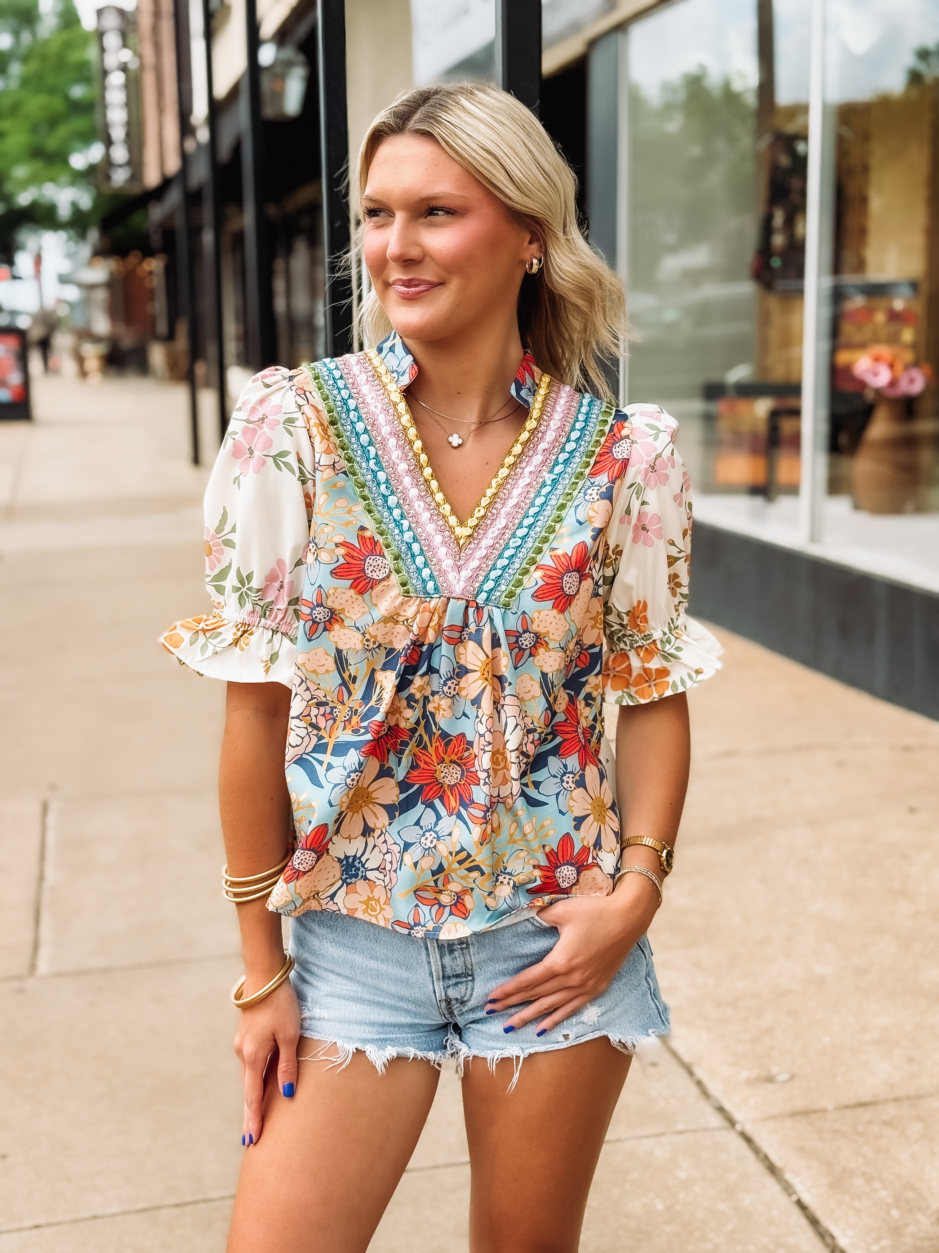 Woman wearing a colorful floral blouse and denim shorts on a sidewalk.