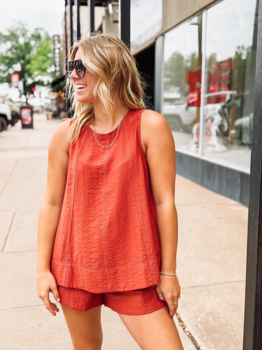 Woman wearing a red sleeveless top and shorts on a city street.