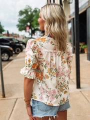 Woman wearing a floral blouse and denim shorts on a sidewalk.